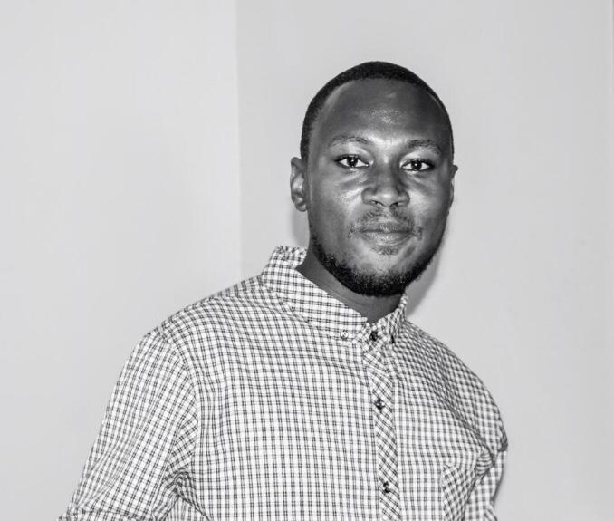 A man in a plaid shirt standing next to a wall.